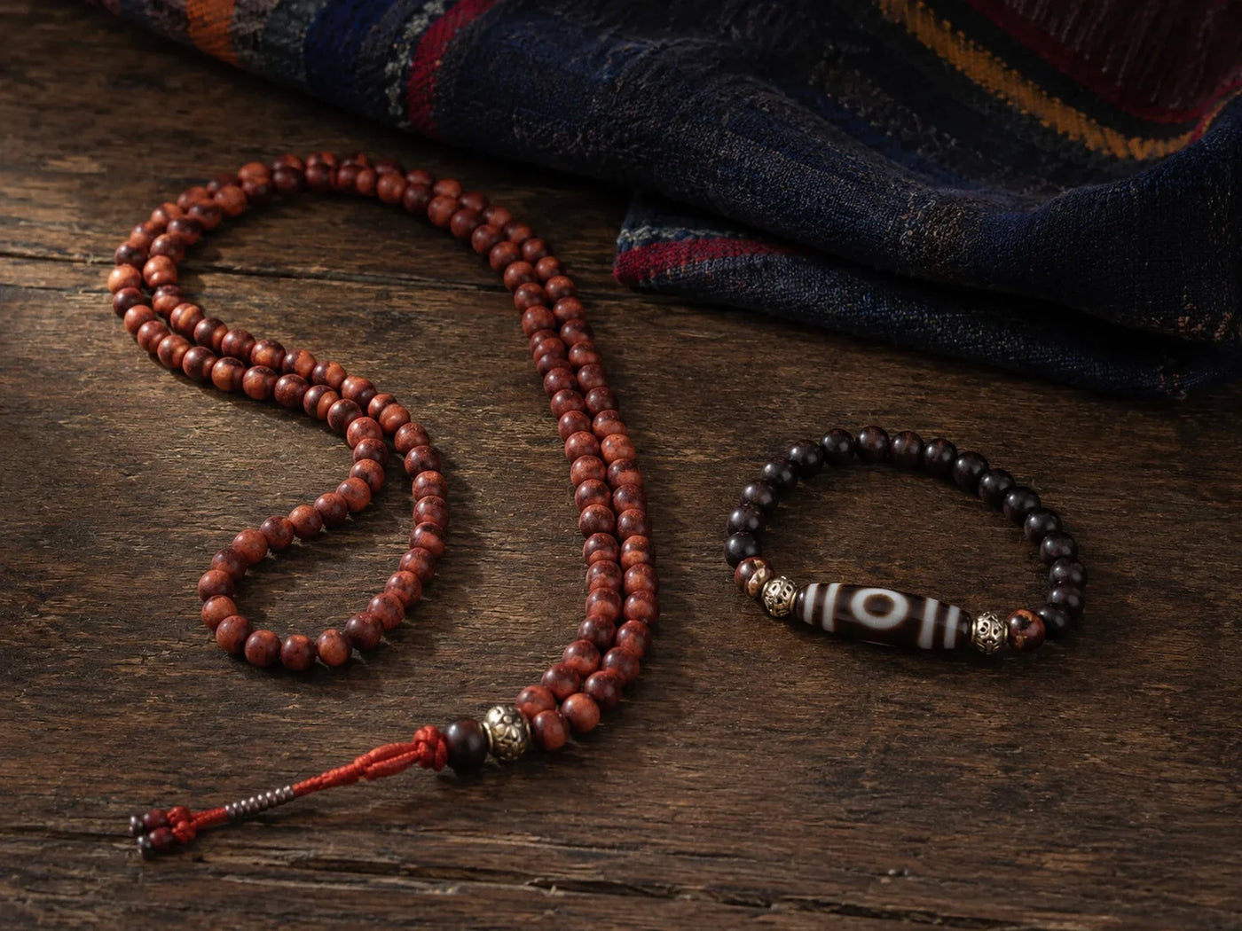 Mala prayer beads and a Dzi bead bracelet arranged side by side on a dark wooden surface