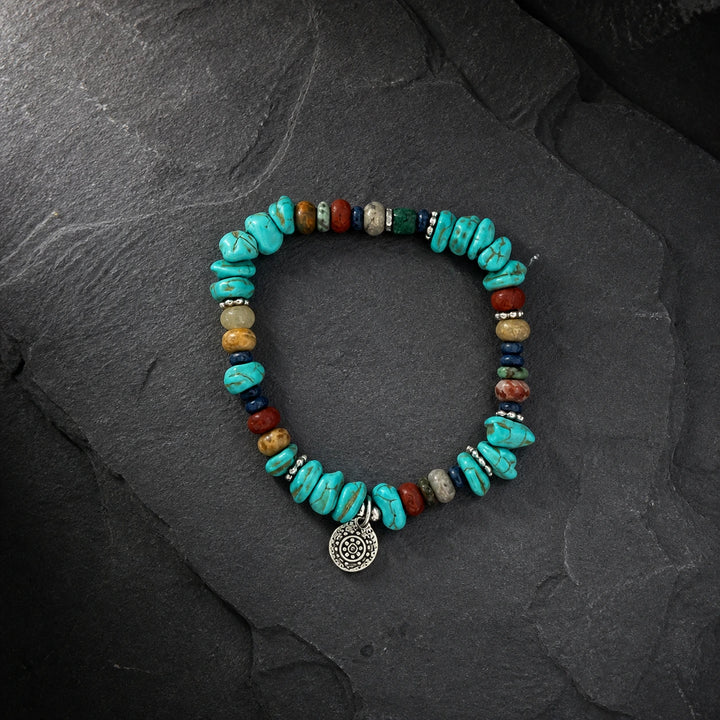 Tibetan-inspired turquoise bracelet with mixed natural stone beads and silver-toned charm on dark stone